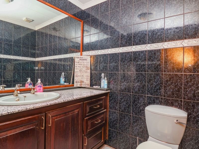 A functional bathroom featuring dark patterned wall tiles, a granite-topped vanity with storage cabinetry, and a large wall-mounted mirror.