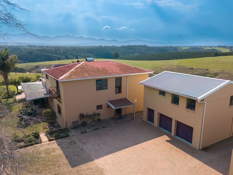 Aerial view of a farm property featuring a main residence with a metal roof, a separate triple garage, and expansive surrounding landscape.