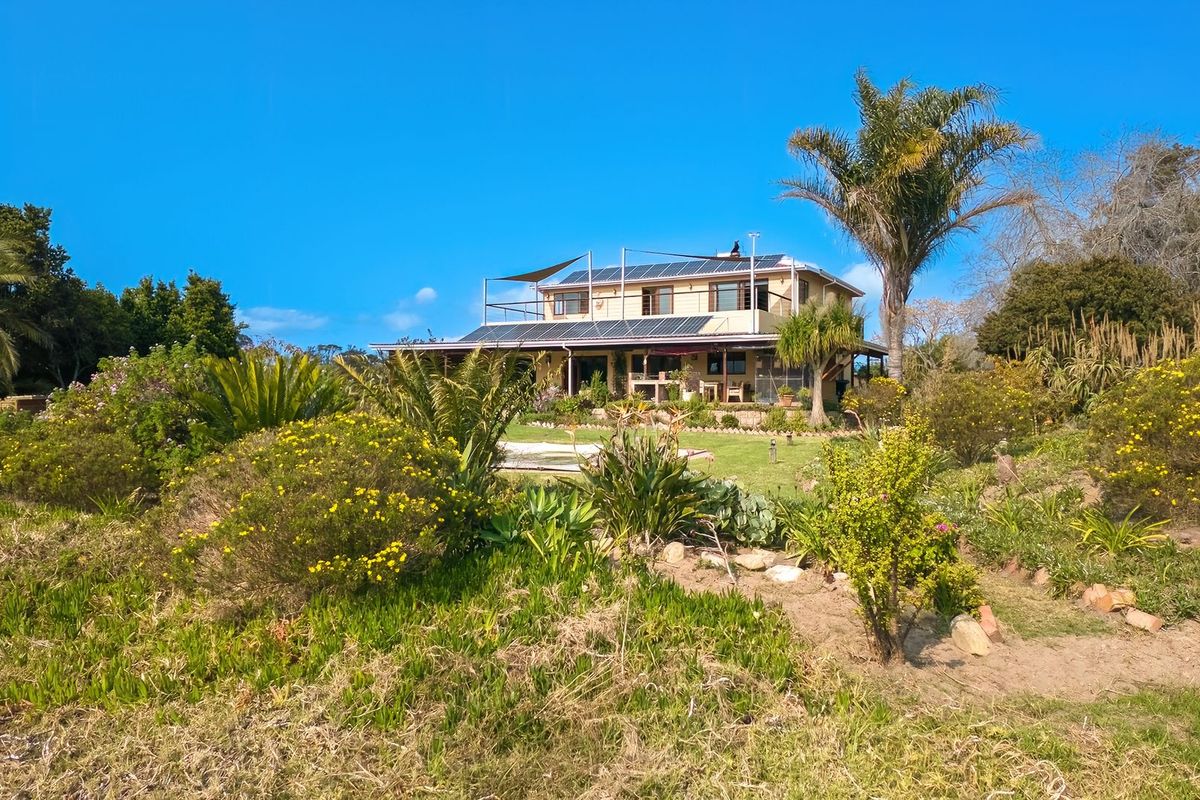 Rear view of a farm property featuring a multi-level structure with solar panels, a roof terrace, and an expansive landscaped garden.