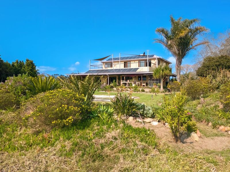 Rear view of a farm property featuring a multi-level structure with solar panels, a roof terrace, and an expansive landscaped garden.