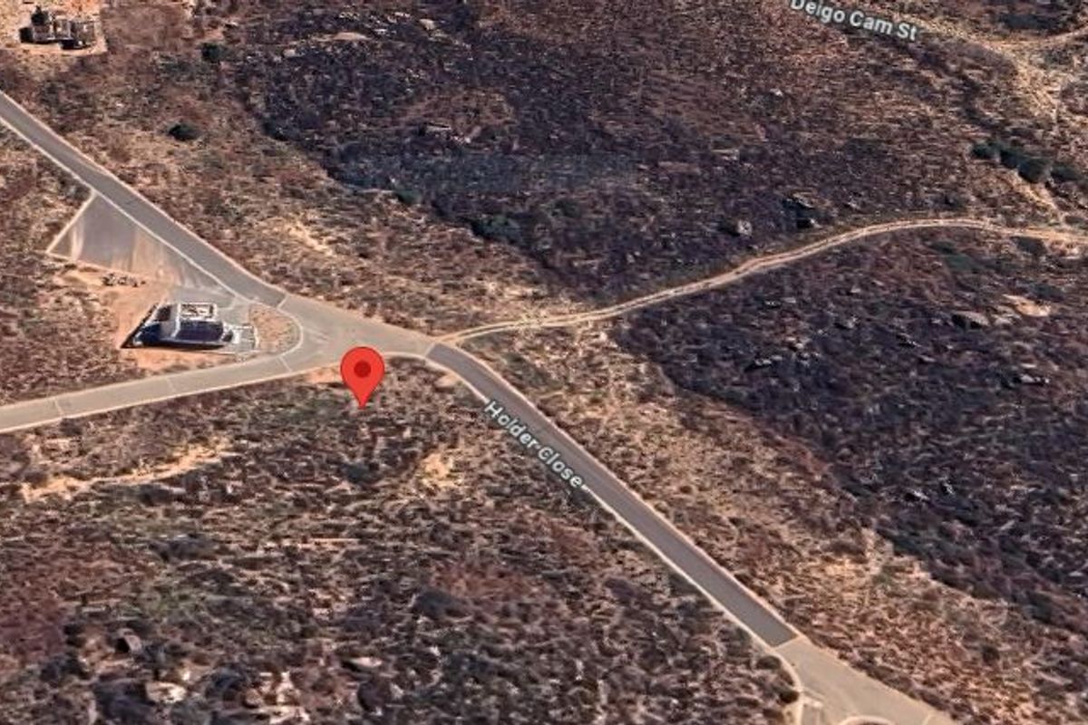 An aerial view of a vacant residential land plot situated at the corner of a paved street in a developing neighborhood.