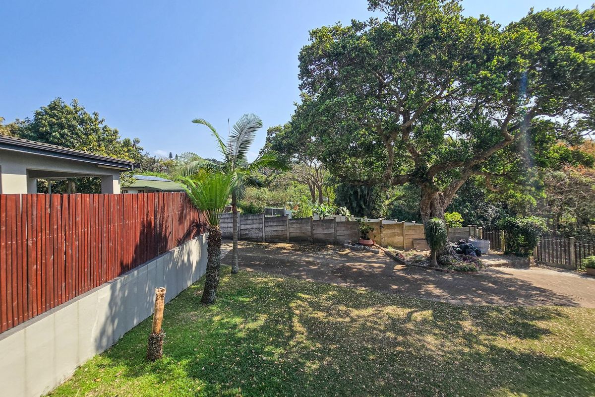 A spacious rear garden area featuring a large mature tree, established lawn, and a combination of timber and concrete boundary fencing.