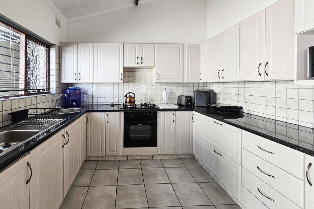 A functional kitchen featuring light-toned cabinetry, dark granite countertops, tiled splashbacks, and a built-in oven with gas hob.