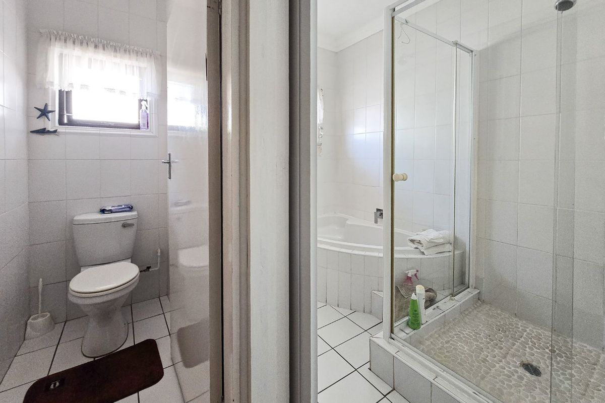 A functional bathroom featuring a separate shower cubicle with pebble-style flooring, a built-in bathtub, and a standard toilet with white wall tiling.