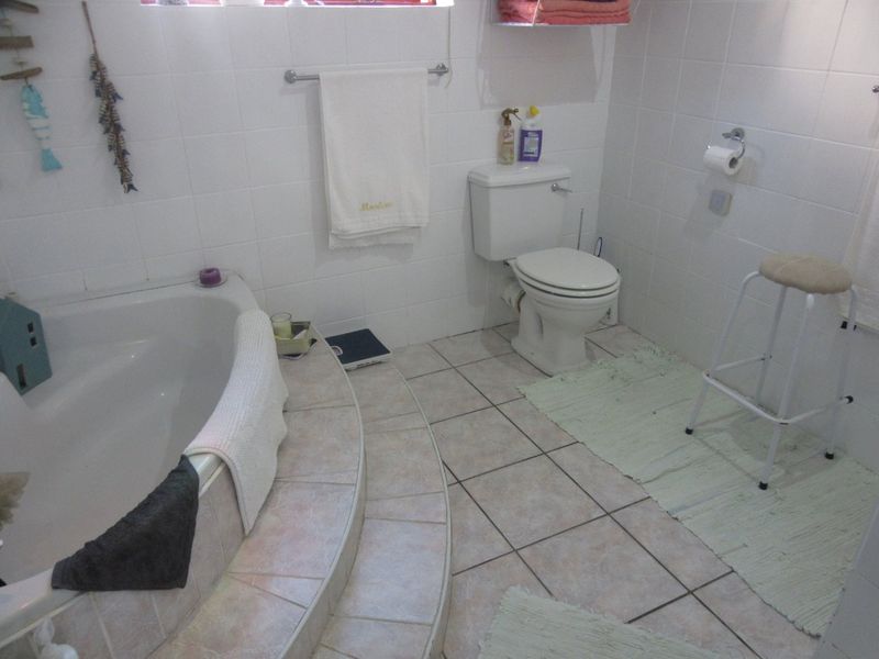 A functional bathroom featuring a built-in corner bathtub with tiled steps, ceramic floor tiling, and standard sanitary fixtures.