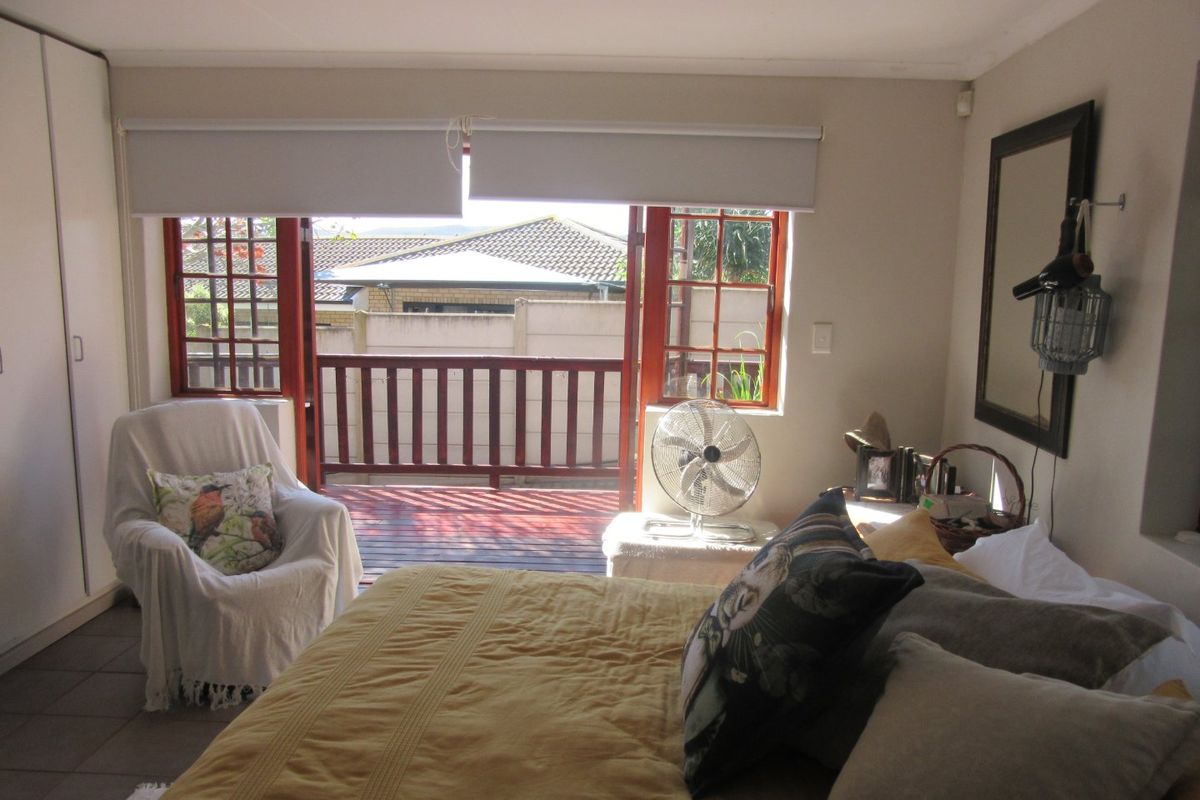 A bedroom featuring tiled flooring, built-in wardrobes, and direct access to a private timber deck balcony through timber-framed doors.