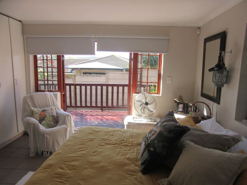 A bedroom featuring tiled flooring, built-in wardrobes, and direct access to a private timber deck balcony through timber-framed doors.