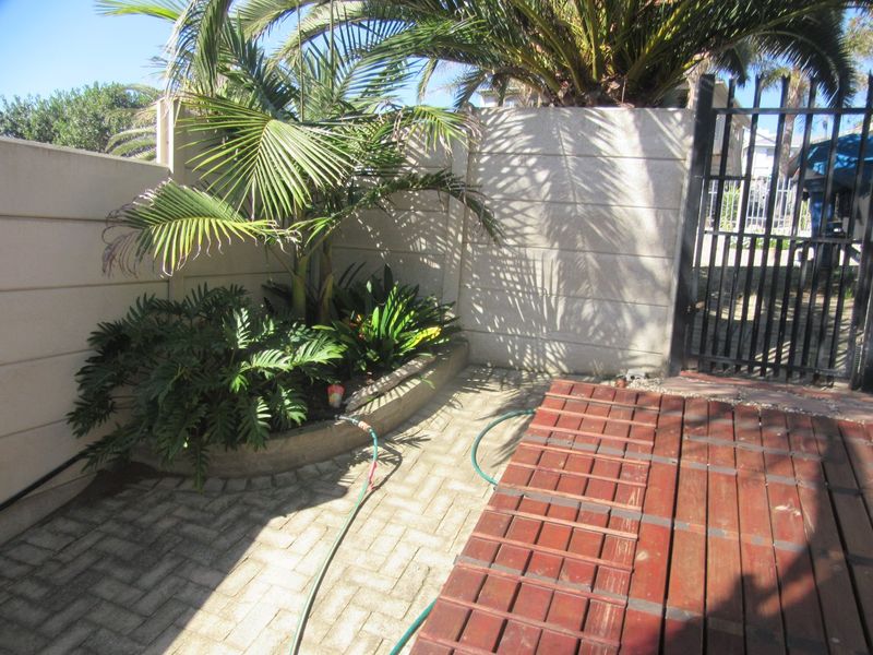 A paved outdoor patio area featuring a raised garden bed, timber decking, and a secure metal gate boundary.