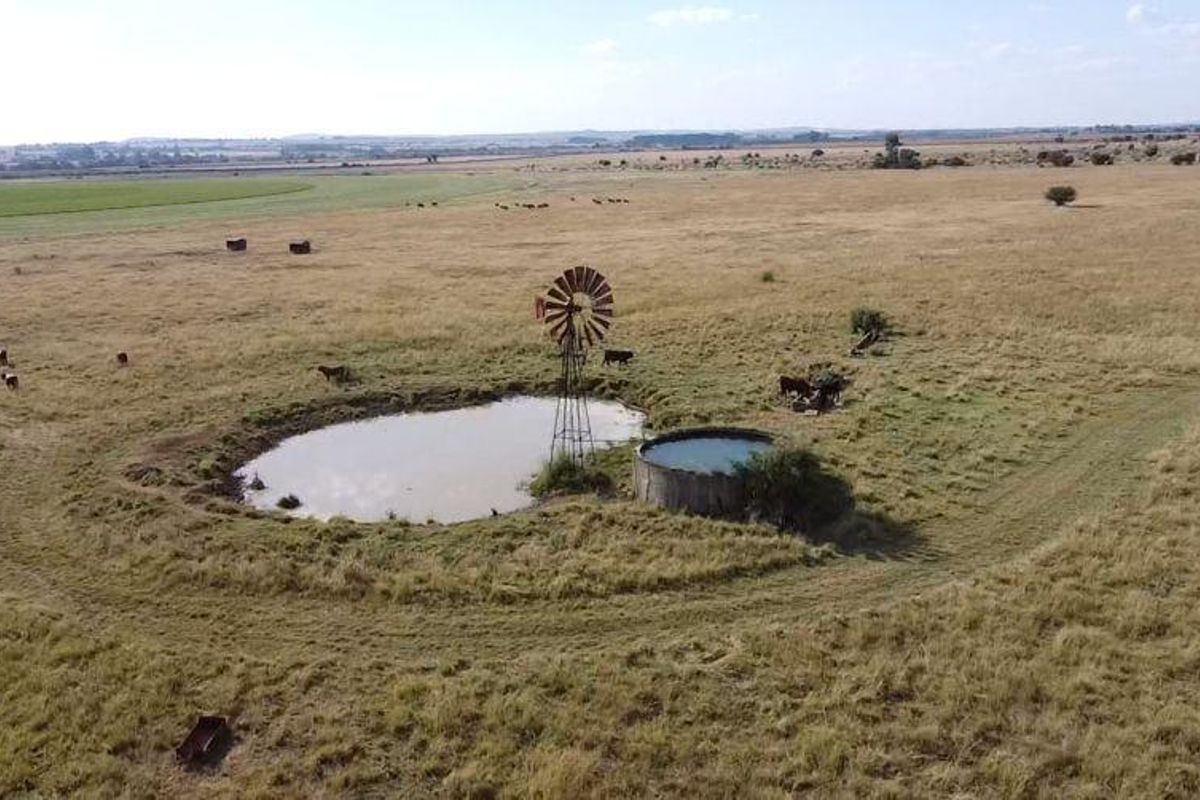 Aerial view of a farm landscape featuring a traditional metal windmill, a natural pond, and a circular concrete water reservoir.