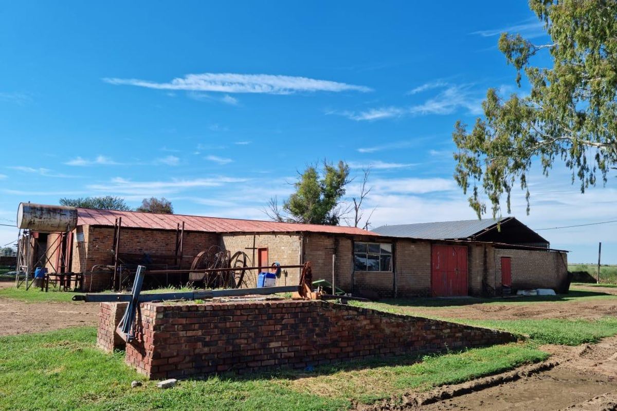 Exterior view of a rustic farm outbuilding featuring brick construction, metal roofing, and a brick loading ramp in a rural setting.