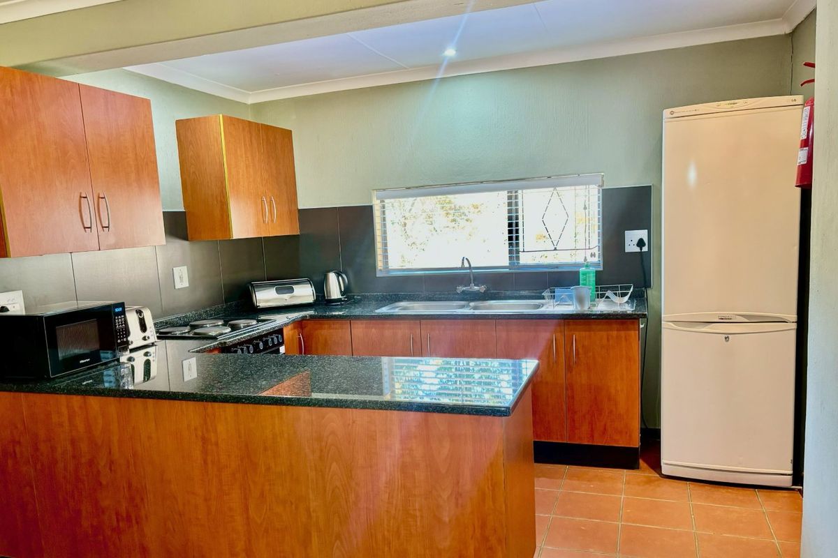 A functional kitchen featuring wood-look cabinetry, granite countertops, a double basin sink, and tiled splashbacks, offering a practical layout for daily use.