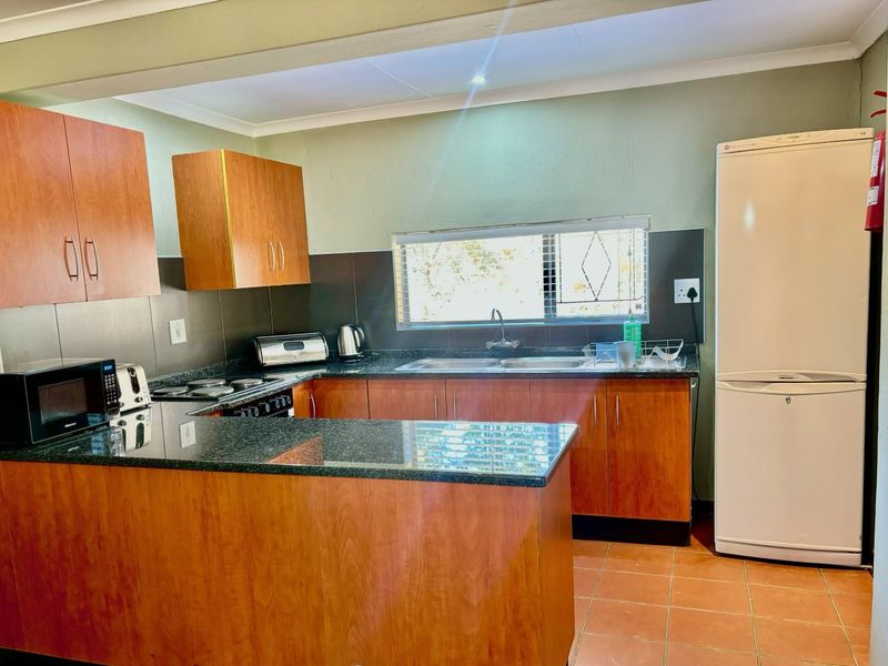 A functional kitchen featuring wood-look cabinetry, granite countertops, a double basin sink, and tiled splashbacks, offering a practical layout for daily use.
