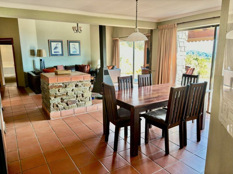 Open-plan living and dining area featuring terracotta floor tiles, a central stone-clad fireplace, and large sliding doors providing access to the outdoor patio.