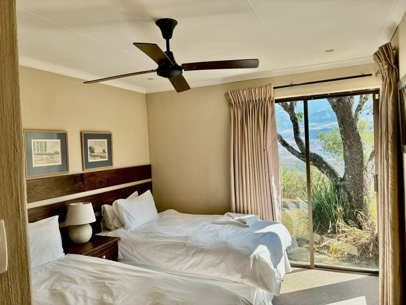 A comfortable bedroom featuring a ceiling fan, built-in headboard, and a large sliding glass door providing natural light and scenic outdoor views.