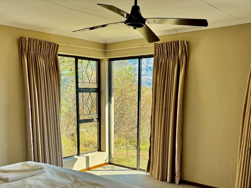 A bedroom featuring a ceiling fan, carpeted flooring, and large sliding glass doors that provide natural light and garden views.