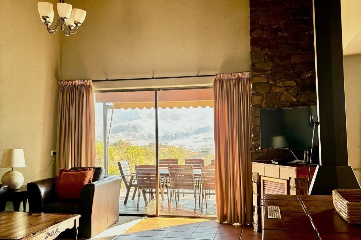 Spacious living room featuring a high exposed timber ceiling, stone fireplace, wood-burning stove, and large sliding doors opening to a scenic outdoor patio.
