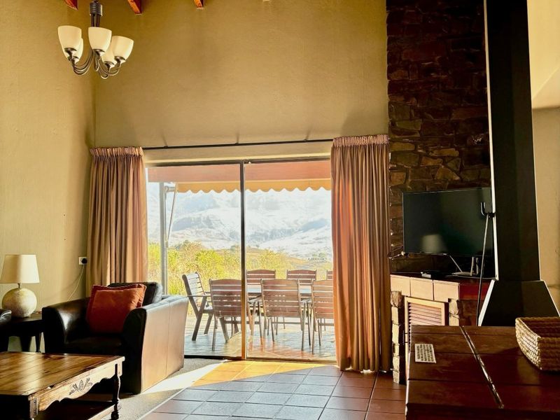 Spacious living room featuring a high exposed timber ceiling, stone fireplace, wood-burning stove, and large sliding doors opening to a scenic outdoor patio.