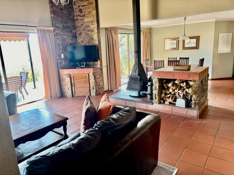 Spacious open-plan living and dining area featuring terracotta flooring, a prominent stone fireplace, and a freestanding wood-burning stove with direct patio access.