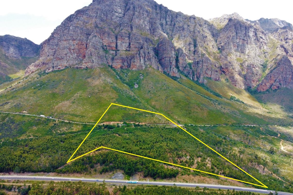 Aerial view of a large, forested farm plot situated against a dramatic mountain backdrop with visible road access.