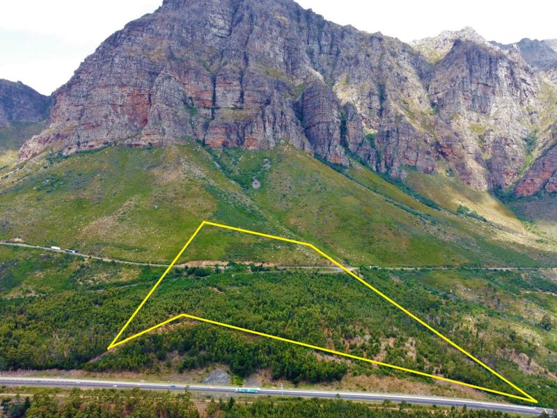 Aerial view of a large, forested farm plot situated against a dramatic mountain backdrop with visible road access.