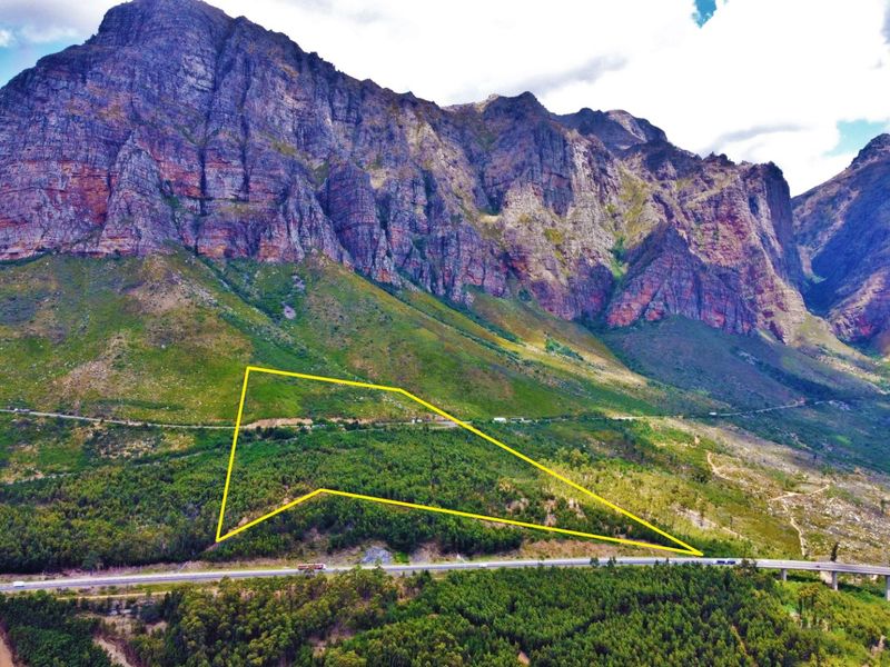Aerial view of a large, forested farm plot situated against a dramatic mountain range, highlighting the property boundaries and natural landscape.