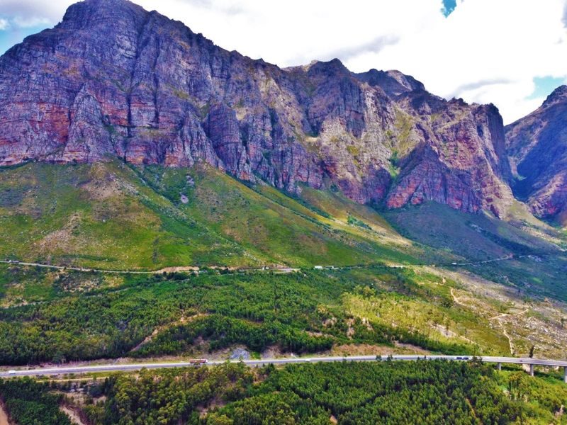 A scenic aerial view of a dramatic mountain range overlooking a lush valley and winding road infrastructure.