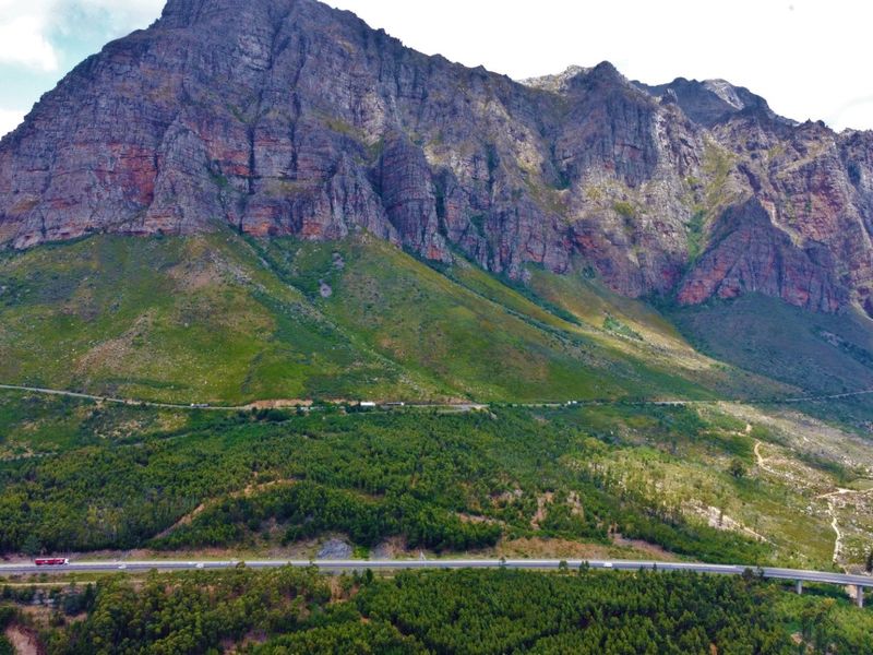 An expansive aerial view of a dramatic mountain range overlooking a lush forest and a winding highway.