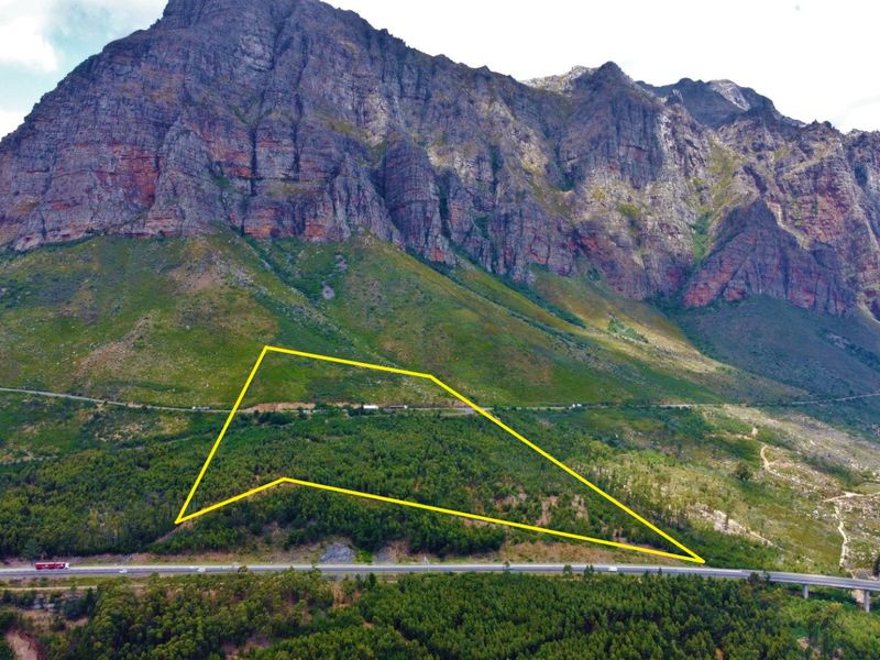 An aerial view of a large, forested farm plot situated against a dramatic mountain backdrop, featuring direct access to a major highway.
