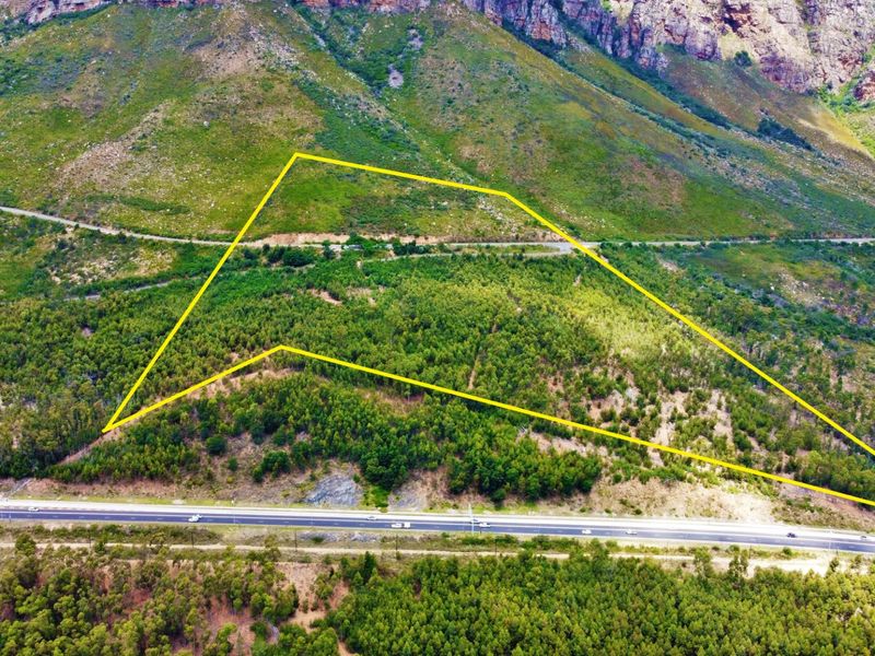 Aerial view of a large, undeveloped farm plot featuring natural vegetation and mountain views, with direct road access.
