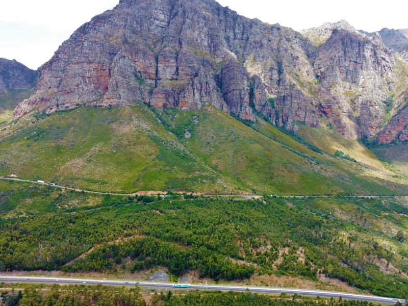 An expansive aerial view of a dramatic mountain range, lush forest, and a winding road, showcasing the natural beauty of the surrounding landscape.