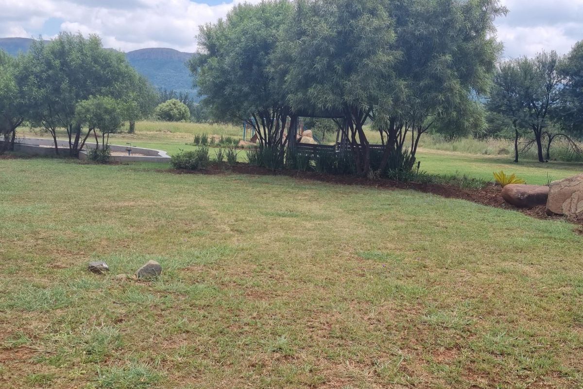 A spacious, well-maintained garden area featuring mature trees, landscaped beds, and scenic mountain views in the background.