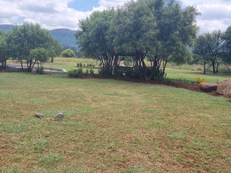 A spacious, well-maintained garden area featuring mature trees, landscaped beds, and scenic mountain views in the background.