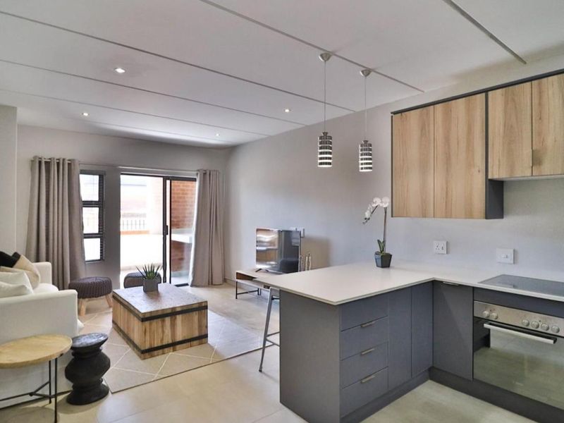 Modern open-plan living area featuring a contemporary kitchen with built-in appliances, stone countertops, and seamless access to a private balcony.