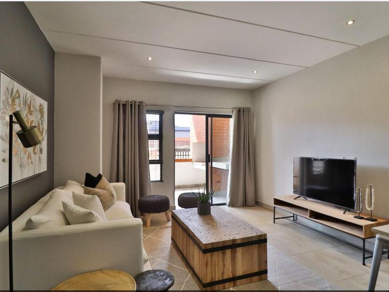 A well-maintained living room featuring tiled floors, recessed lighting, and a sliding glass door providing access to an outdoor balcony area.