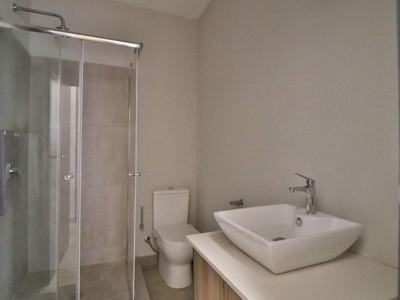 A modern, clean bathroom featuring a glass-enclosed shower, a contemporary vessel sink on a vanity cabinet, and a standard toilet.