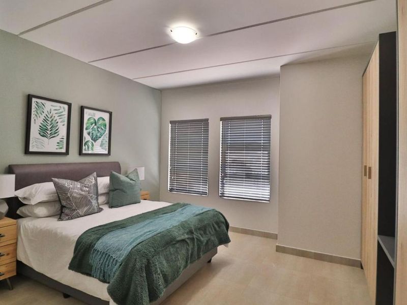 A well-maintained bedroom featuring neutral tiled flooring, built-in wardrobe storage, and dual windows fitted with venetian blinds.