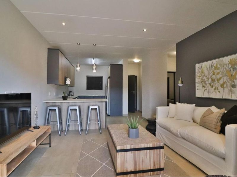 Modern open-plan living area featuring a contemporary kitchen with breakfast bar, stone countertops, and sleek cabinetry, seamlessly flowing into the lounge space.