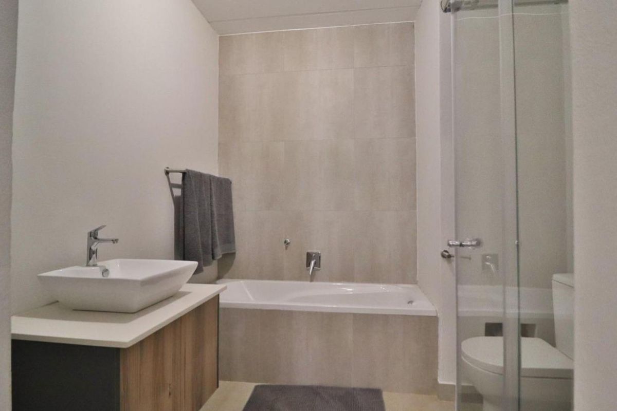 A modern bathroom featuring a vessel sink on a vanity cabinet, a built-in bathtub with tiled surround, and a separate glass-enclosed shower area.