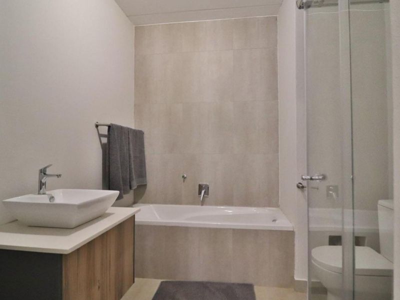 A modern bathroom featuring a vessel sink on a vanity cabinet, a built-in bathtub with tiled surround, and a separate glass-enclosed shower area.