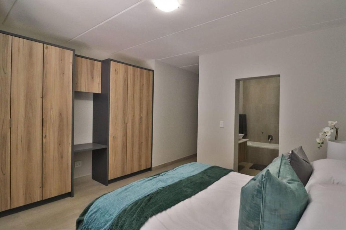 A modern bedroom featuring built-in wooden cupboards with an integrated desk and direct access to an en-suite bathroom.