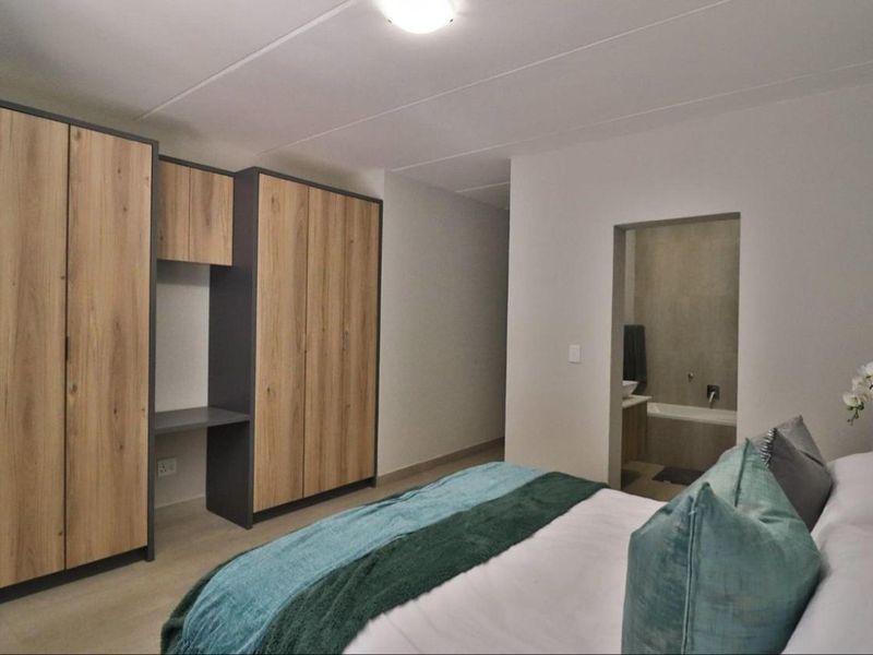 A modern bedroom featuring built-in wooden cupboards with an integrated desk and direct access to an en-suite bathroom.