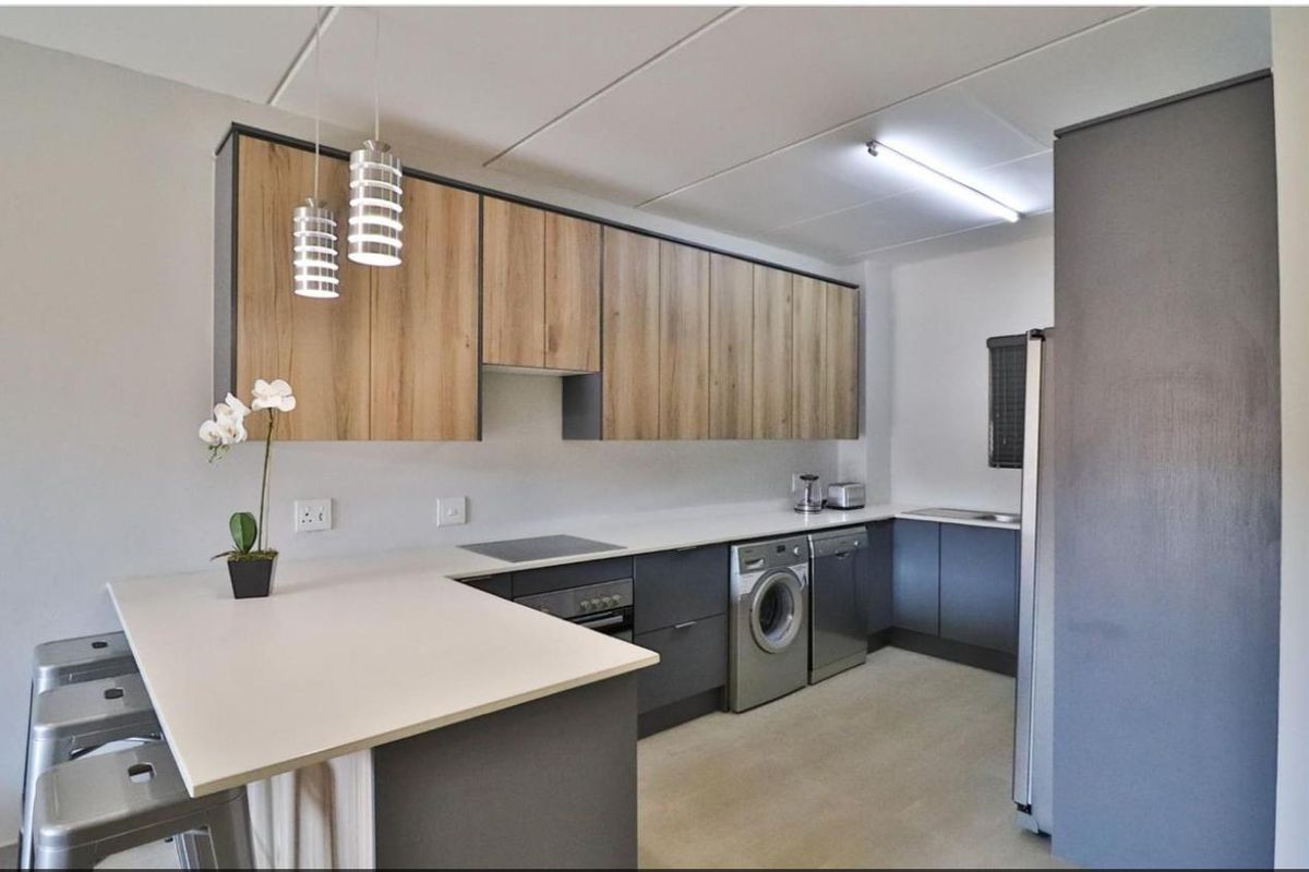 Modern kitchen featuring two-tone cabinetry, stone countertops, integrated appliances, and a breakfast bar with pendant lighting.