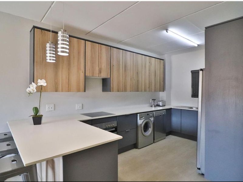 Modern kitchen featuring two-tone cabinetry, stone countertops, integrated appliances, and a breakfast bar with pendant lighting.