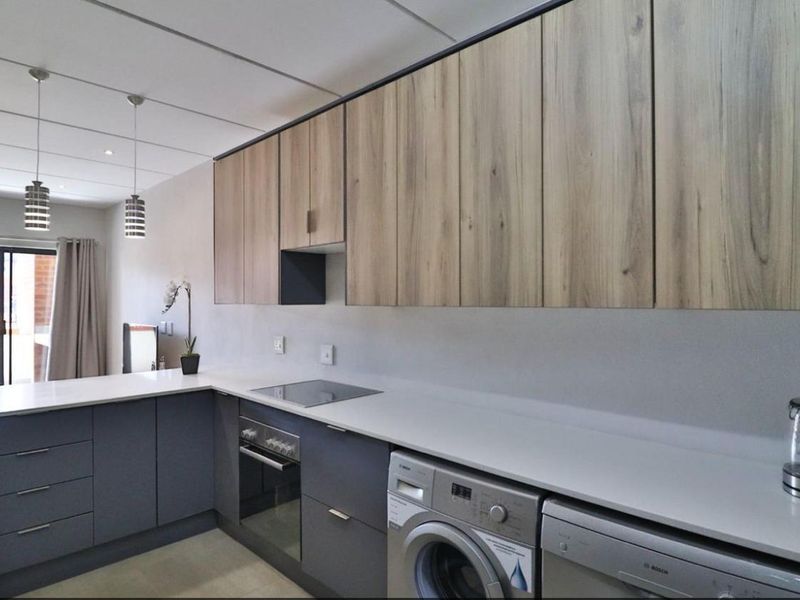 Modern kitchen featuring sleek grey lower cabinetry, light wood-grain upper cabinets, stone countertops, and integrated appliances including an oven, hob, and laundry facilities.