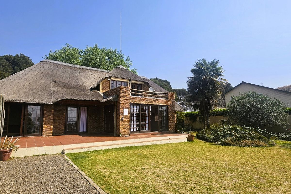 Rear view of a traditional face brick house featuring a thatch roof, spacious tiled patio, and a well-maintained garden area.