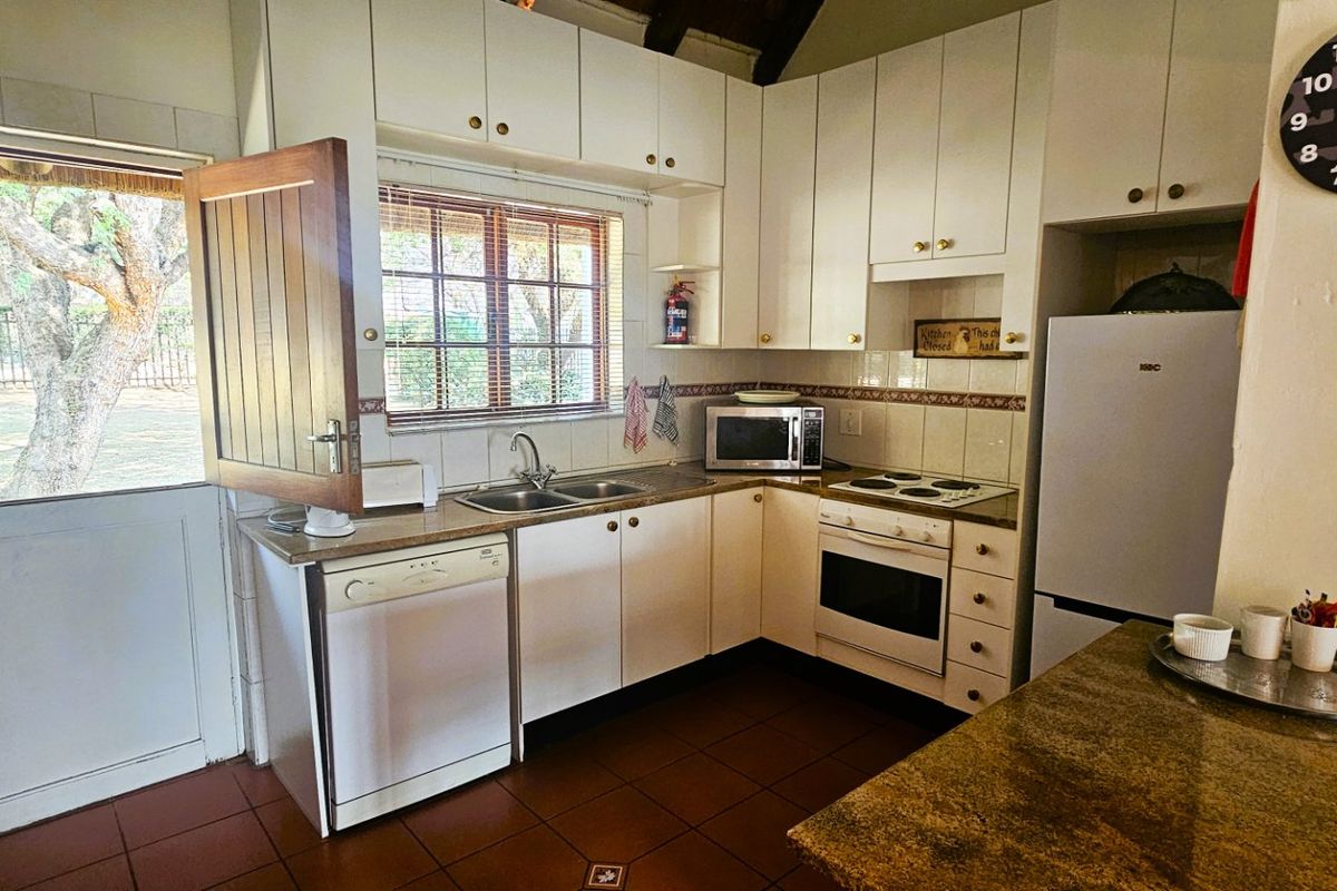 A functional kitchen featuring white cabinetry, tiled flooring, a built-in oven and hob, and direct access to the garden via a stable door.