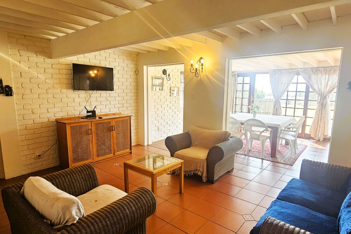 A cozy living room featuring exposed beam ceilings, painted brick walls, and terracotta floor tiles, with direct access to an adjoining patio area.