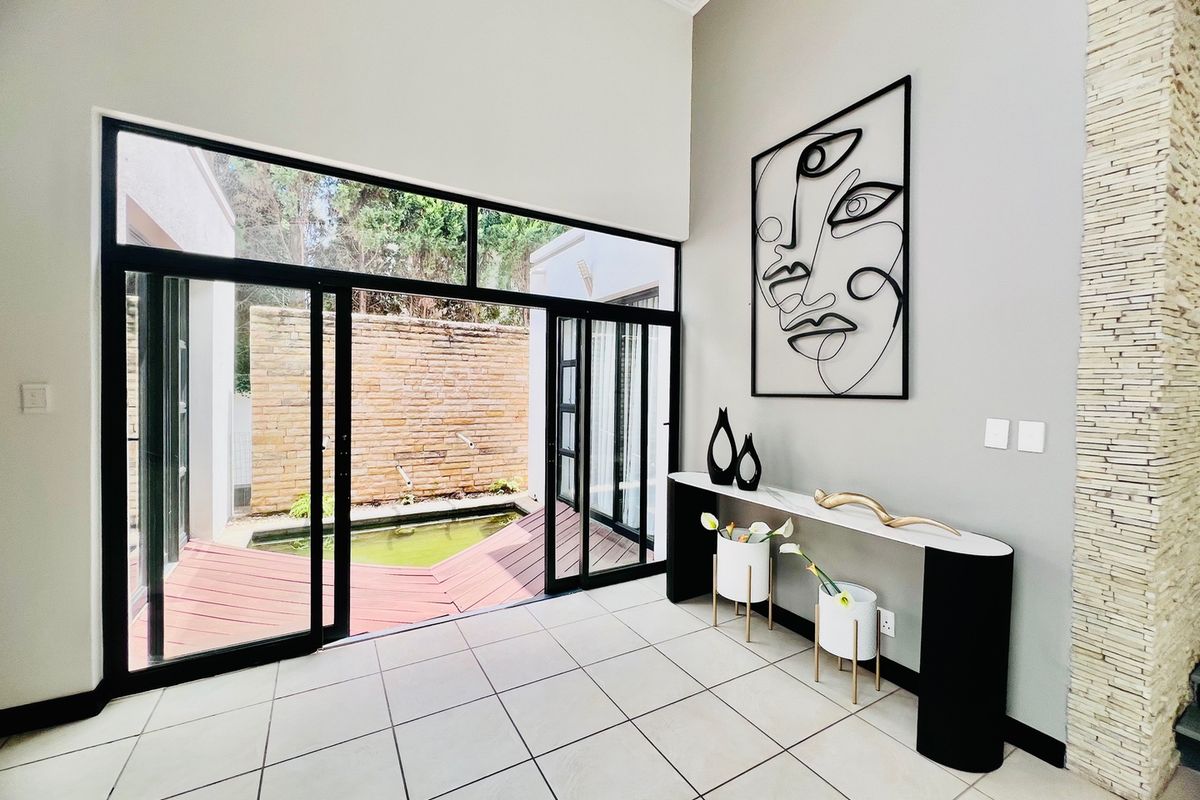 Bright living area featuring high ceilings, large sliding glass doors opening to a courtyard with a water feature, and a decorative stone wall.