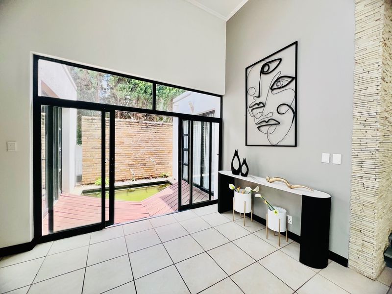 Bright living area featuring high ceilings, large sliding glass doors opening to a courtyard with a water feature, and a decorative stone wall.