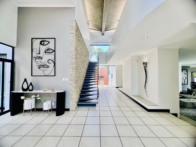 Spacious modern entrance hall featuring high vaulted ceilings, a striking feature stone wall, and a contemporary floating staircase leading to the upper level.